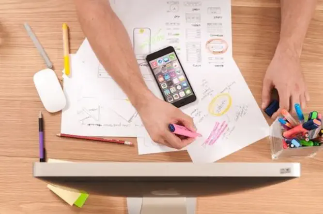 Designer working on a mobile design with smarphone, papers, and a laptop